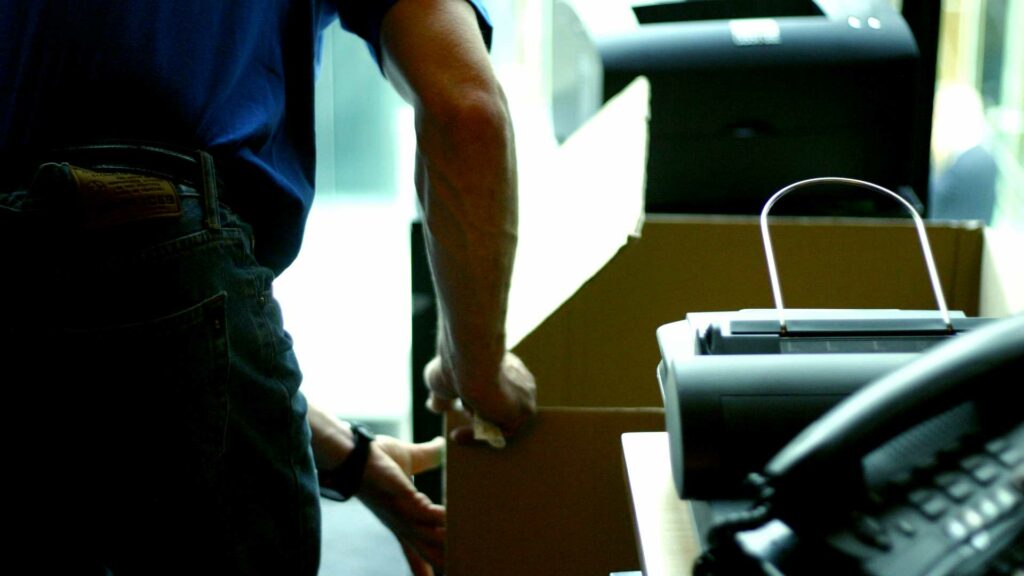 Personne ouvrant une boîte ou récupérant des documents dans un emballage près d’une imprimante.