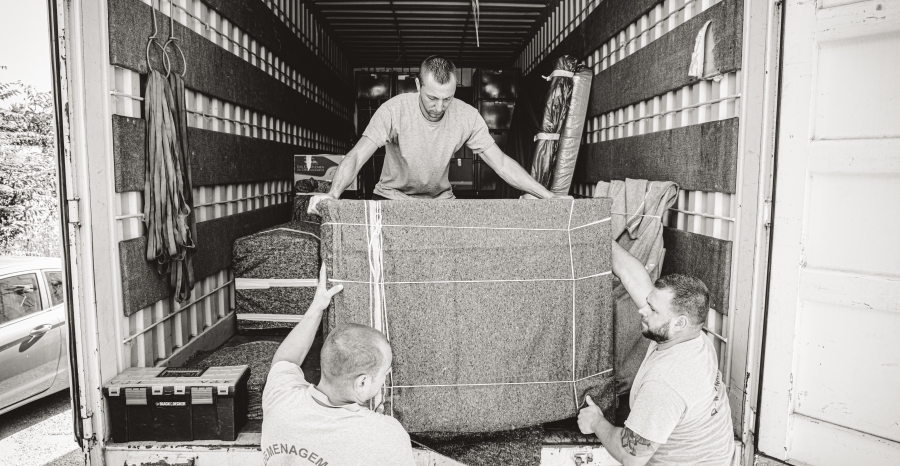 Trois personnes déplacent et manutentionnent un grand meuble emballé dans un camion de déménagement.